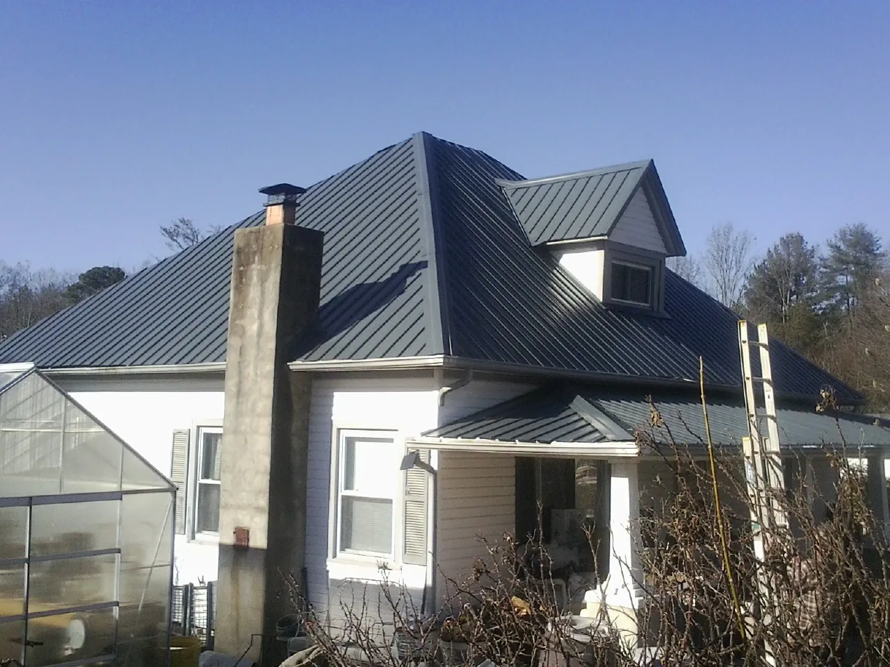 Dark blue standing seam metal roof on a white farmhouse with dormer — Slate & Tile Roof Repair by Roofing Brothers in Helper