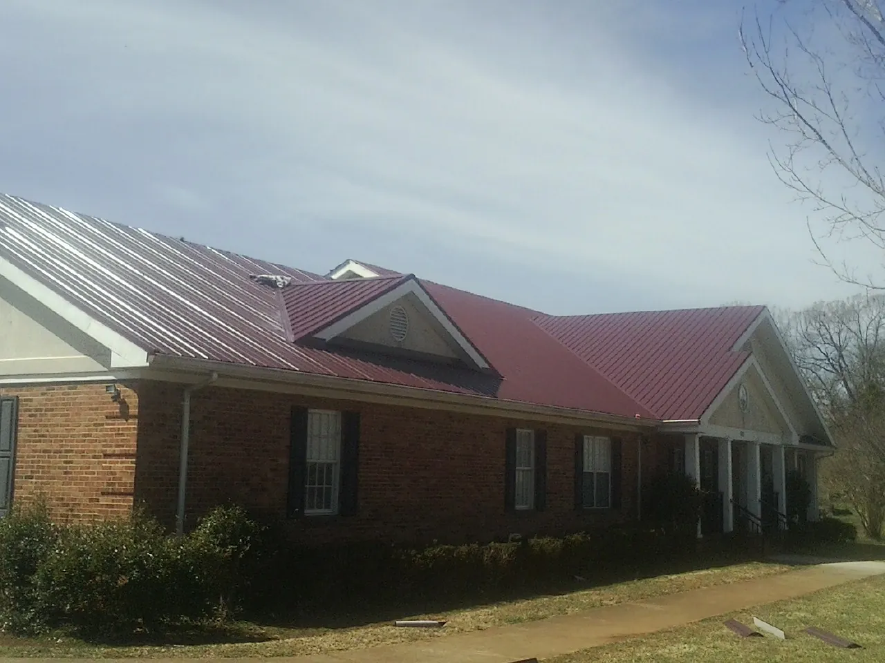 Red metal roof with gabled entries on a long brick building, from a Hail Damage Roof Repair job in Helper
