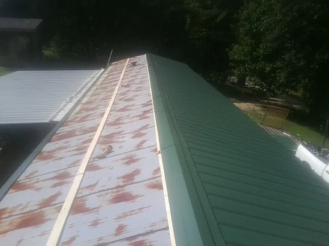 Old rusted panels beside newly installed green metal roofing — Wind Damage Roof Repair by Roofing Brothers in Helper