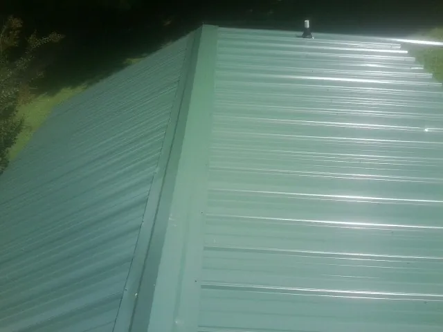 New green metal panels meeting at the ridge of a roof — Flat Roof Repair work by our crew in Helper