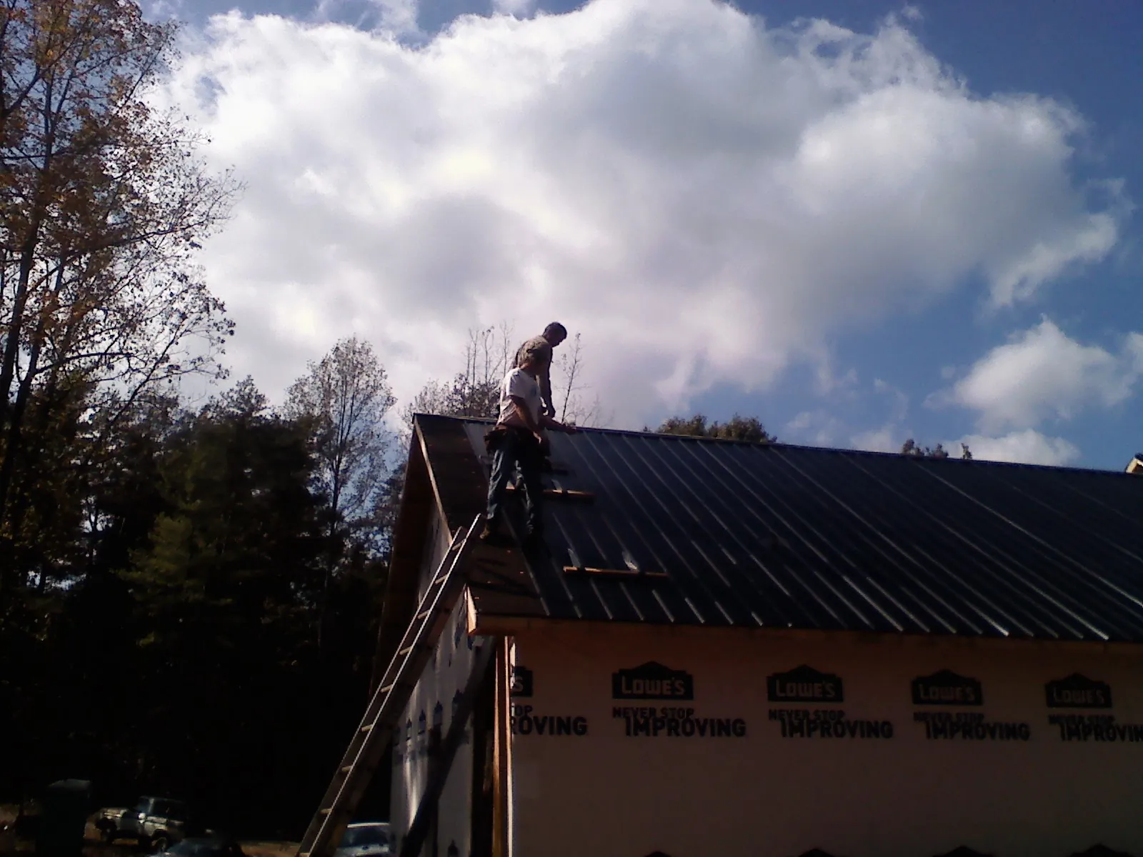 Roofer fastening dark metal panels high against a cloudy sky, from a Roof Inspection job in Helper