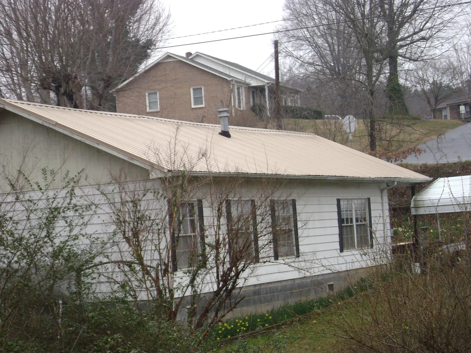 Tan metal roof on a white sided house set into a hillside — Commercial Roofing by Roofing Brothers in Helper